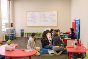Group leader wearing purple engages a diverse group of participants seated in a circle on a carpeted floor