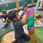 Toddler stacking colorful magnetic tiles at San Leandro, California preschool